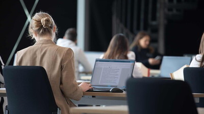 Eine konzentrierte Kandidatin bearbeitet ihr digitales juristisches Staatsexamen am Laptop, mit Gesetzestexten in der Nähe, in einem professionellen digitalen Prüfungsumfeld.