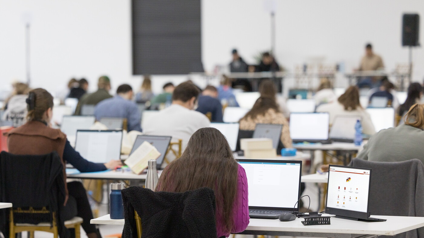 Rechtsreferendarinnen und Rechtsreferendare schreiben das Zweite Staatsexamen in Rheinland-Pfalz am Laptop, daneben ein zweiter Bildschirm mit der digitalen Examensbibliothek