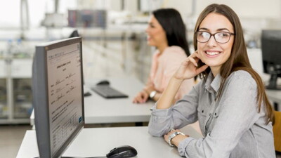 Eine glückliche Studentin blickt auf ihren Laptop, während sie die Prüfungseinsicht mit der Software Q-Exam durchführt.