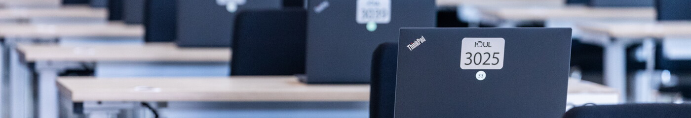 Ein ordentlicher Prüfungsraum mit sauber angeordneten Schreibtischen, auf denen aufgeklappte Laptops für die bevorstehende E-Prüfung bereitstehen.