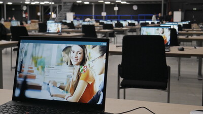 Ein Laptop zeigt die Login-Maske für eine E-Prüfung, bereit für den Prüfungsstart, in einem hellen, organisierten Prüfungsraum.