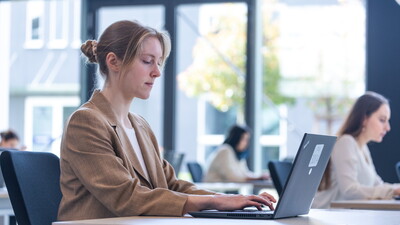 Eine Kandidatin sitzt vor einem Prüfungslaptop während des E-Exams im Jura (1. Staatsexamen). Zu sehen ist die IQUL Software Q-Exam, die für die Durchführung der Prüfung verwendet wird. Die Kandidatin tippt eifrig in die Prüfung.