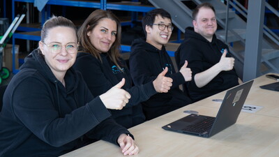 Vier Prüfungsleiter zeigen den Daumen hoch und überwachen eine geordnete E-Prüfung, während die Kandidat ruhig an ihren Laptops arbeiten.